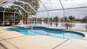 Ein Pool mit geschwungener Kante, umgeben von einer überdachten Fläche mit Blick auf einen See und Häuser im Hintergrund.