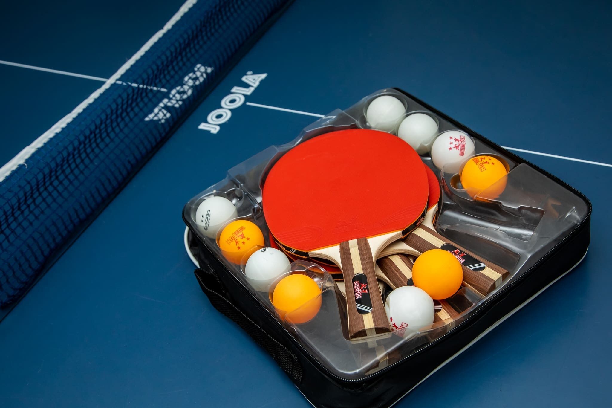 A table tennis table with a blue net and a table tennis paddle set on it.