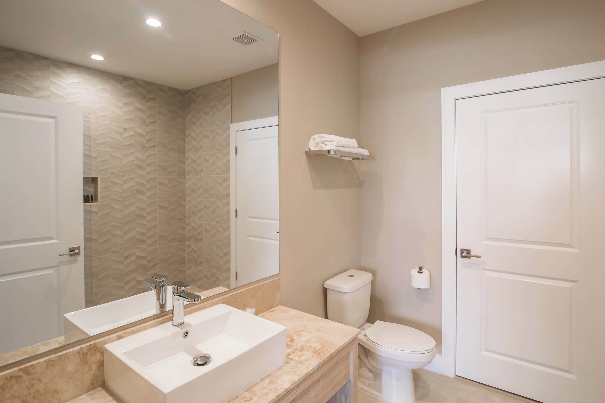 A modern bathroom with a large mirror, a sink, a toilet, and a towel rack.