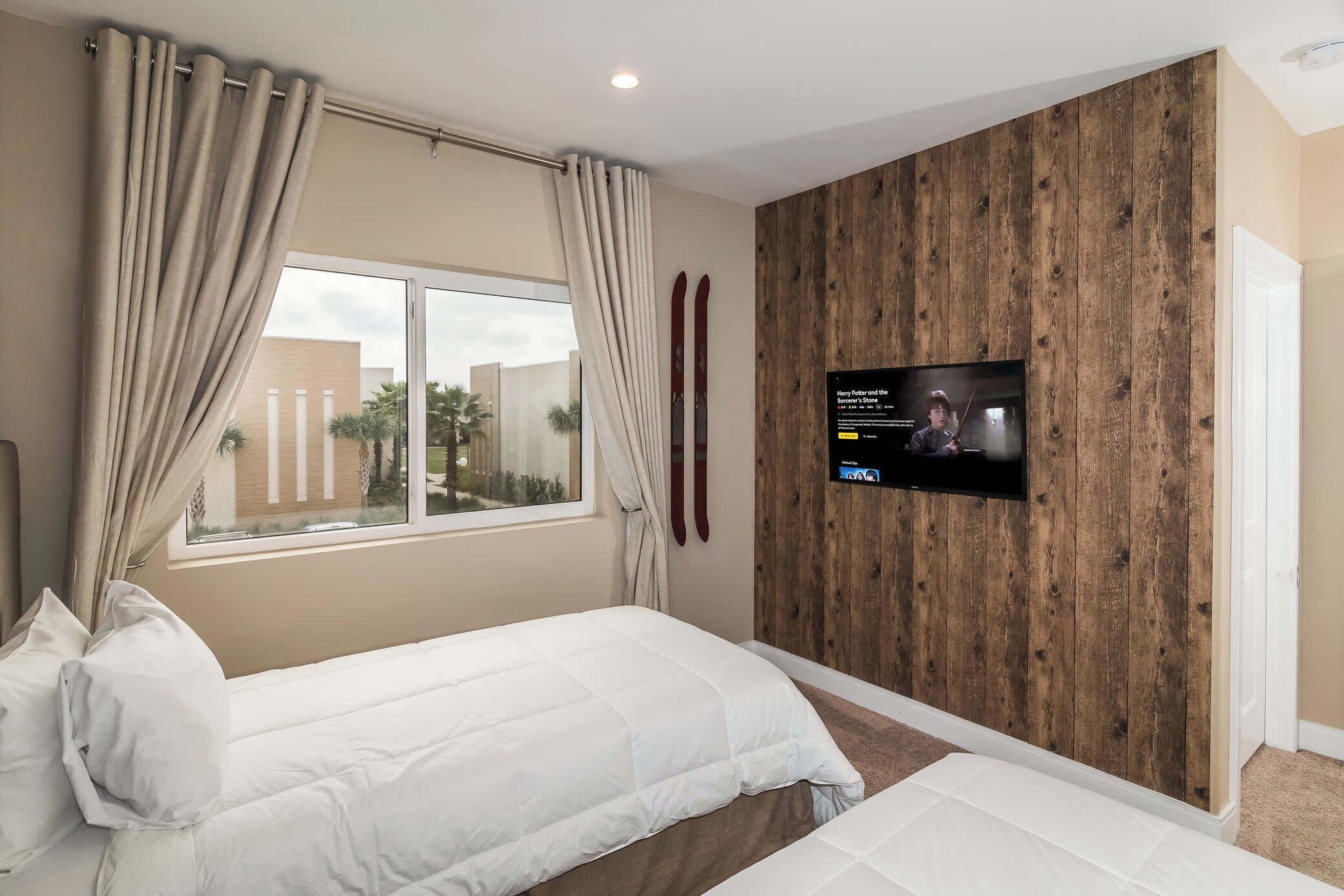 Habitación de hotel con dos camas, un televisor instalado en una pared de madera y una ventana con cortinas.