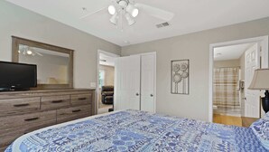 A bedroom with a large bed, a wooden dresser, a ceiling fan, and a television. - Valley View Retreat - Holiday Hills Branson - Golf Resort -outdoor Pools (Branson)