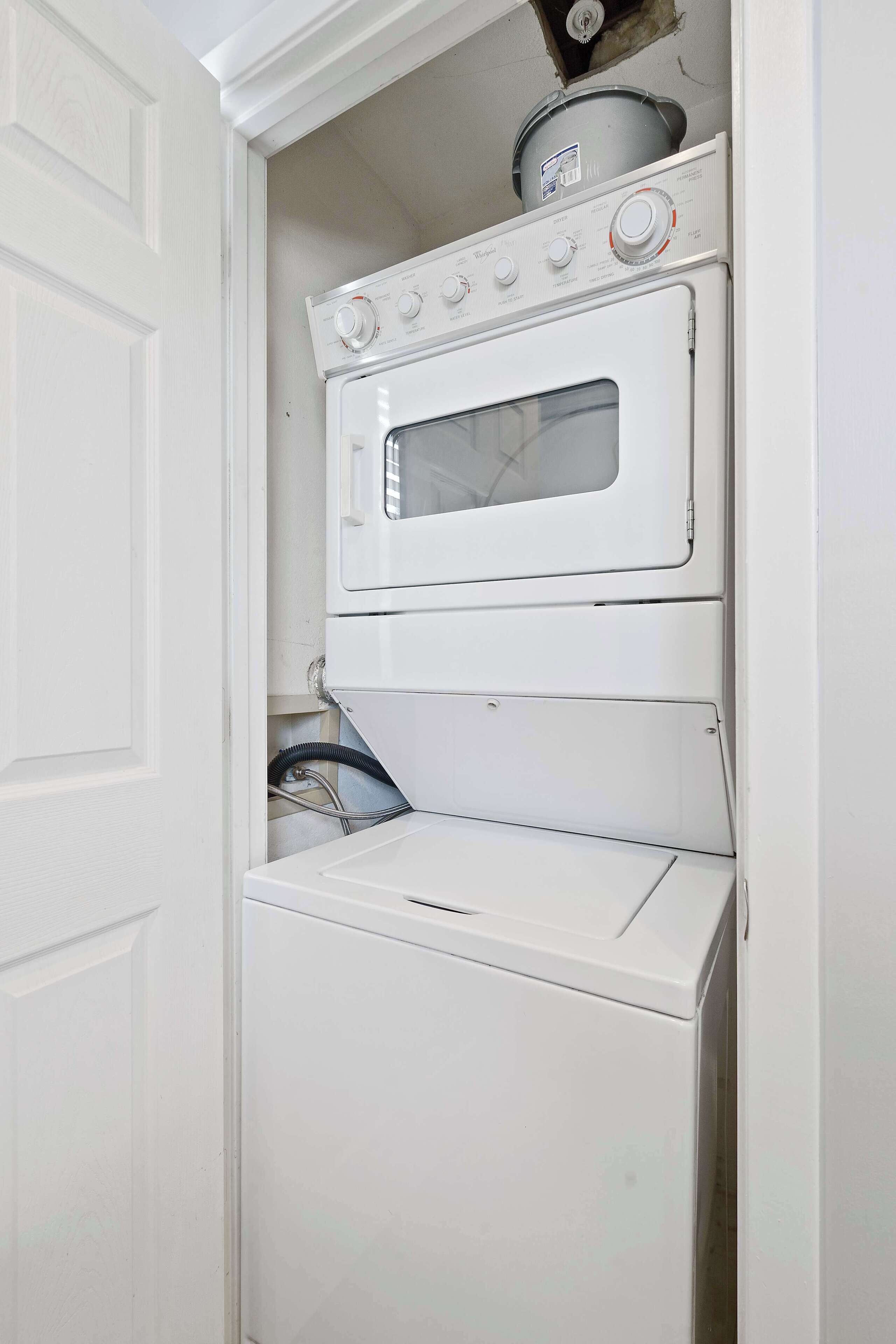 A compact laundry room with a stacked washer and dryer, a small oven, and a visible water pipe.