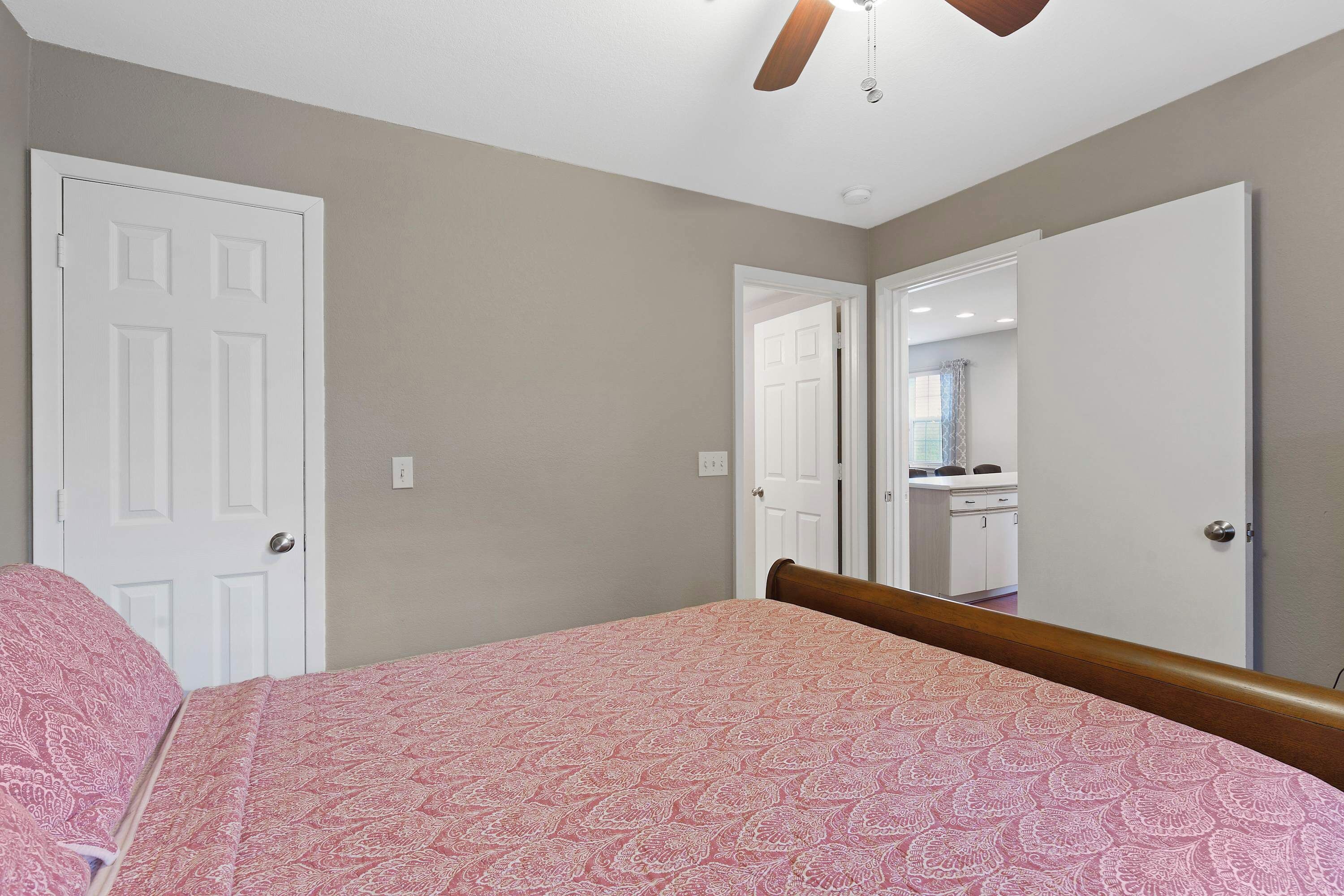 A bedroom with a bed, a ceiling fan, and a door leading to a bathroom.