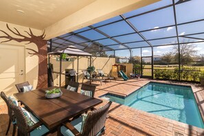 Un espace extérieur abrité comprenant une piscine, une table à manger avec des chaises et un barbecue.