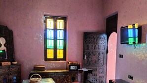 A traditional room with a bed, a window with colorful stained glass, a television, and a decorative door. - JNANE GHMATE (marrakech)