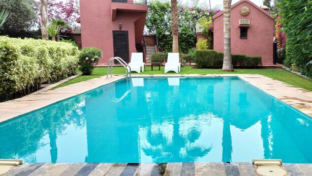 A rectangular swimming pool with clear blue water, surrounded by a tiled deck. There are two white lounge chairs and a small table in the background. - JNANE GHMATE (marrakech)