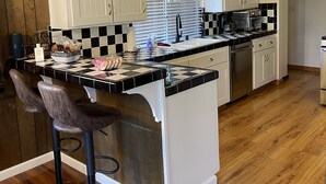 A modern kitchen with white cabinets, a black and white checkered backsplash, and a wooden floor. - 3 bedroom dream home 🏡 Big Bear Lake CA / Running Springs/Lake Arrowhead. (Running Springs)