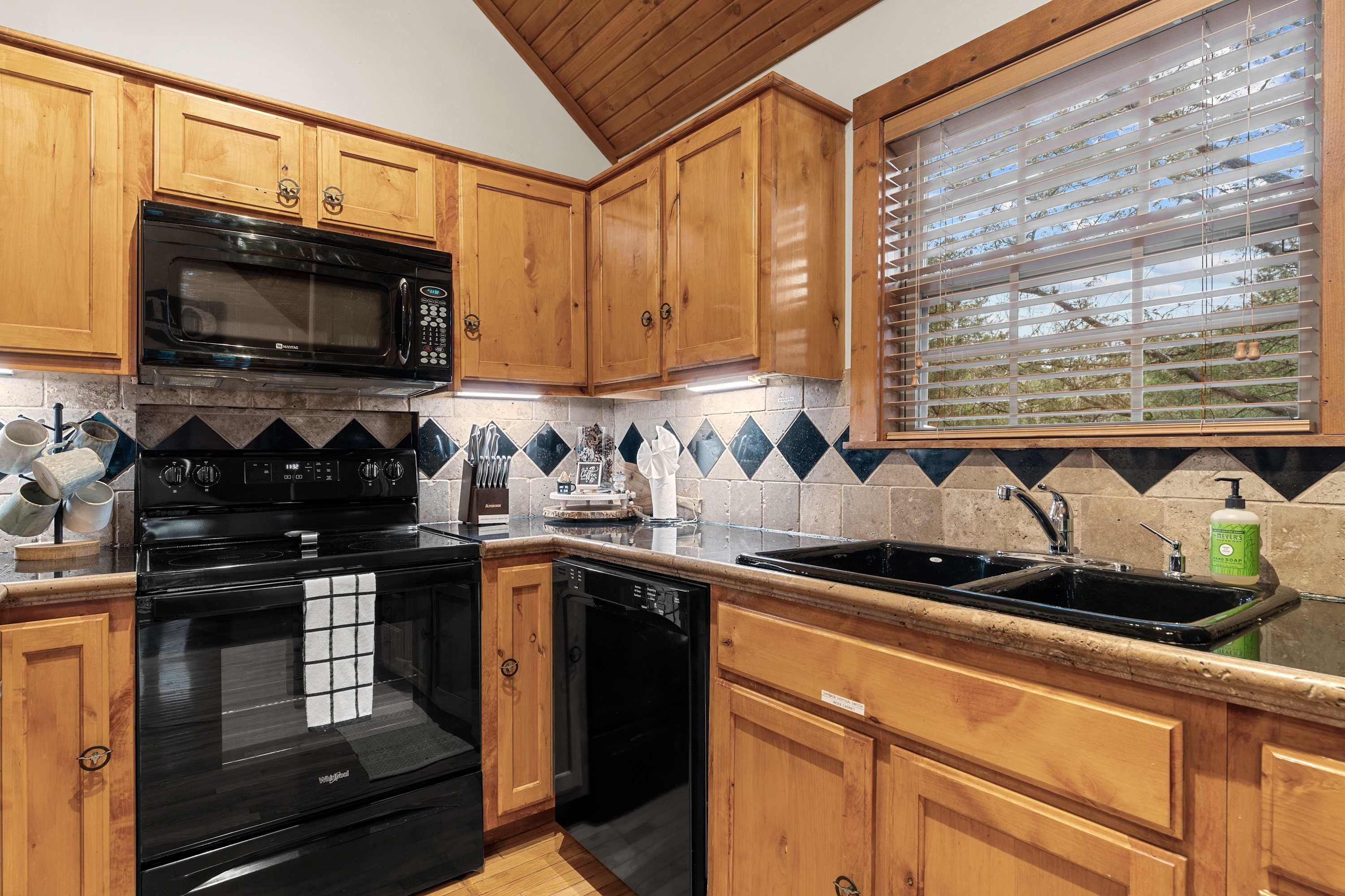 A kitchen with wooden cabinets, a black microwave, a stove, a dishwasher, a sink, and a window with blinds.