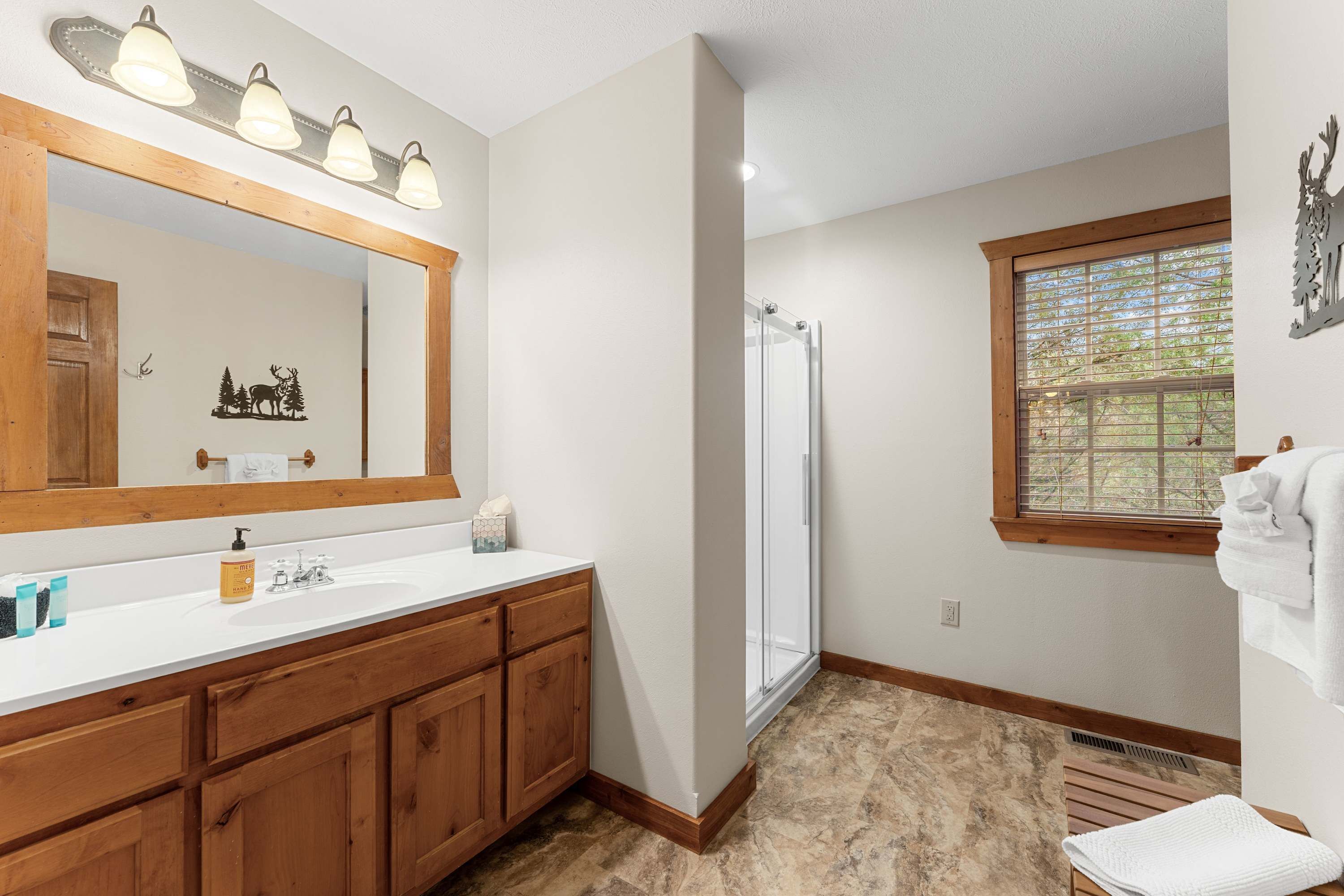 A bathroom with a wooden vanity, a large mirror, a shower, and a window with a view.