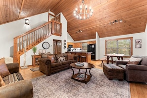 A spacious living area with a wooden staircase, a dining table, and a kitchen area.