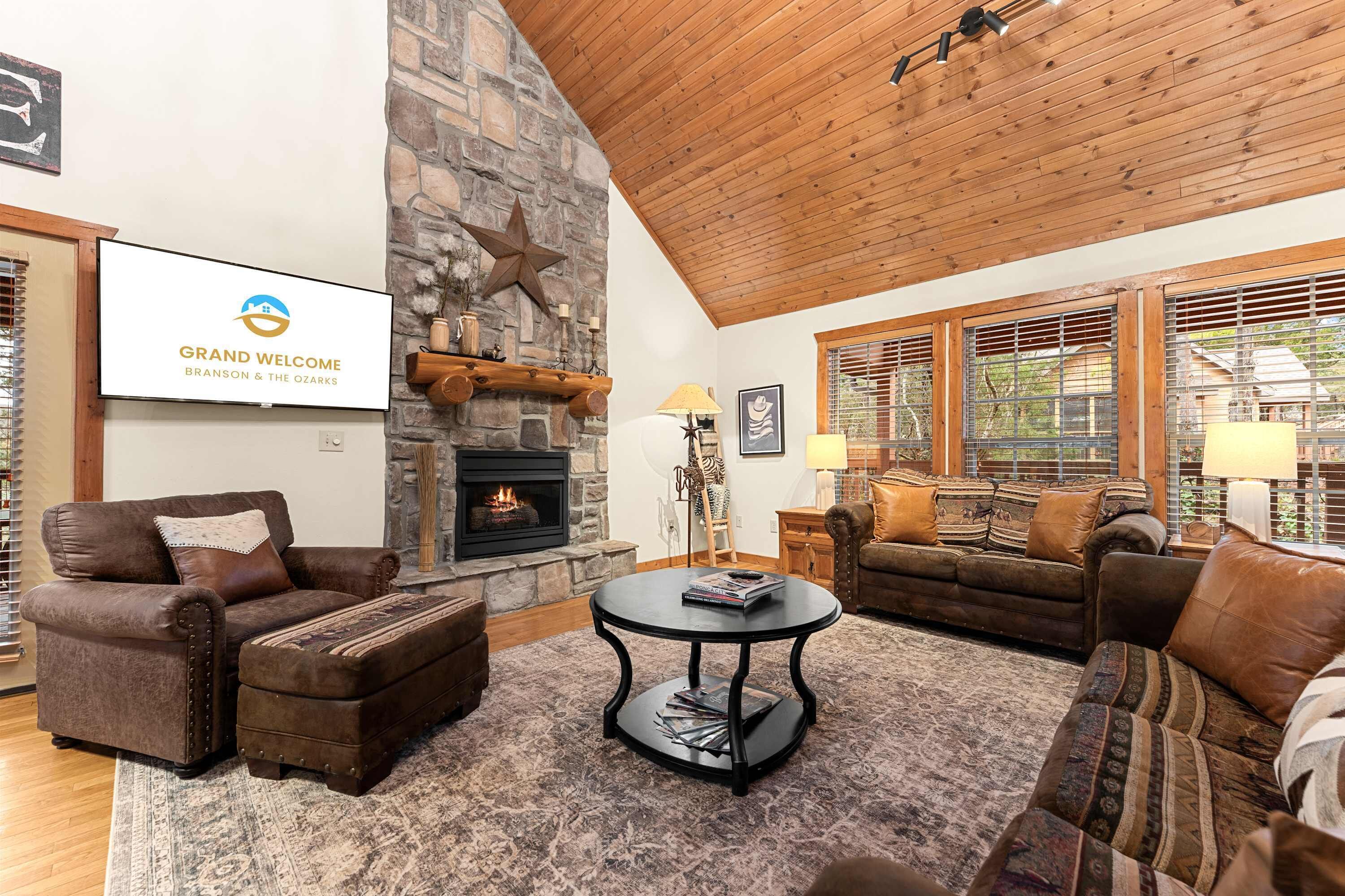 A cozy living room with a stone fireplace, leather furniture, and a large window with blinds.