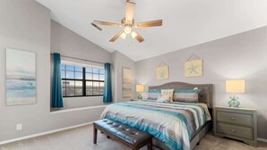 A bedroom with a bed, bench, ceiling fan, bedside tables, and artwork.