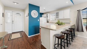 A modern kitchen with white cabinets, a blue accent wall, a clock, and a bar area with stools.