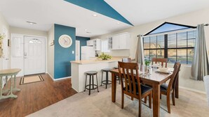 A modern kitchen with white cabinets, a central island, and a dining area with wooden chairs and a table.