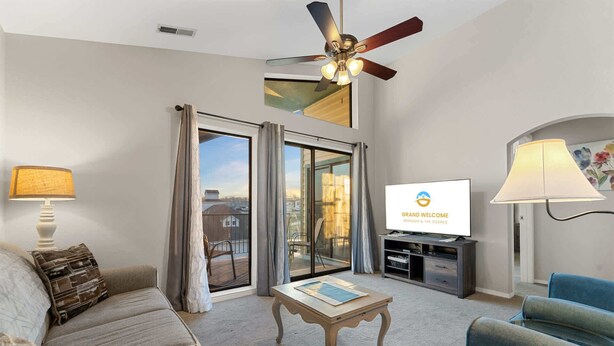 A hotel room with a sofa, a coffee table, a TV, a ceiling fan, and a view through the glass doors.