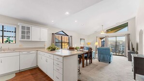 A modern kitchen with white cabinets, a dining area with a table and chairs, and a large sliding glass door leading to a balcony.