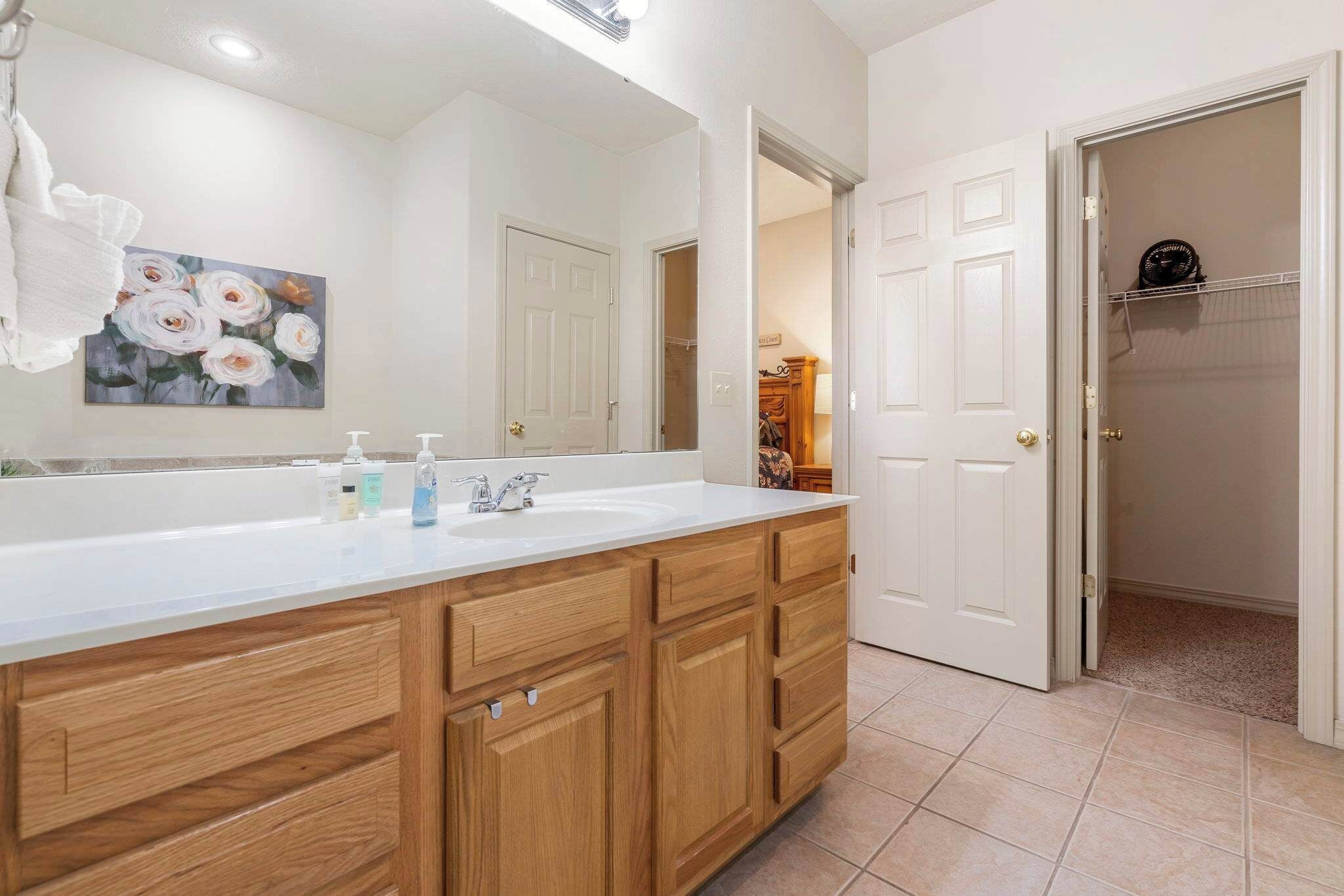A bathroom with a wooden vanity, a large mirror, and a painting of flowers.