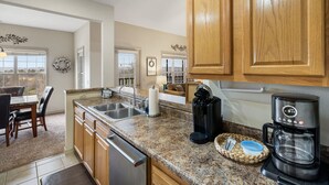 A kitchen with granite countertops, wooden cabinets, a coffee maker, and a dishwasher. - The Gathering Place - Minutes to 61-acre Theme Park (Branson West)