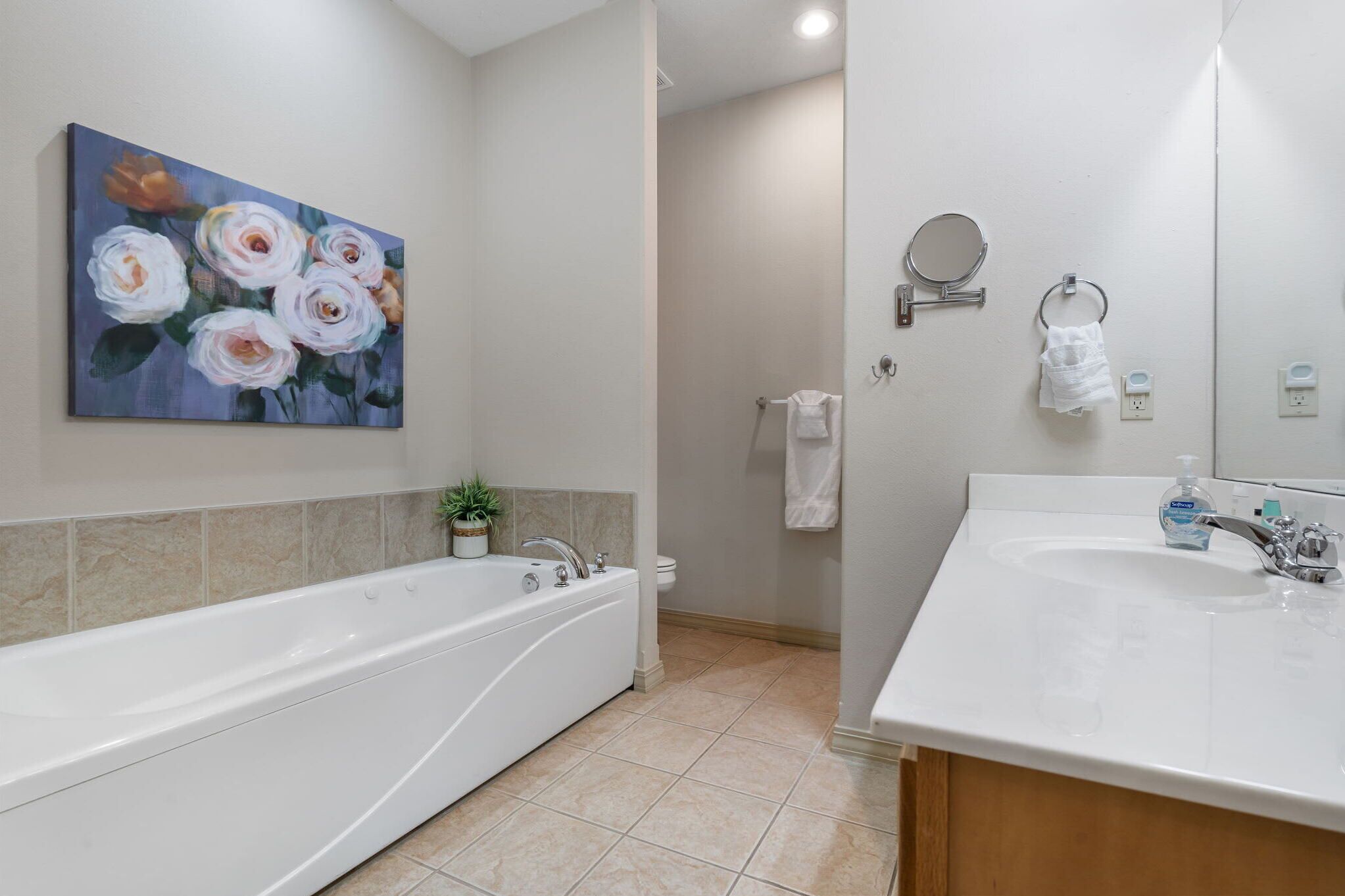 Un baño moderno con una bañera grande, un lavamanos, un espejo y un cuadro de flores en la pared.