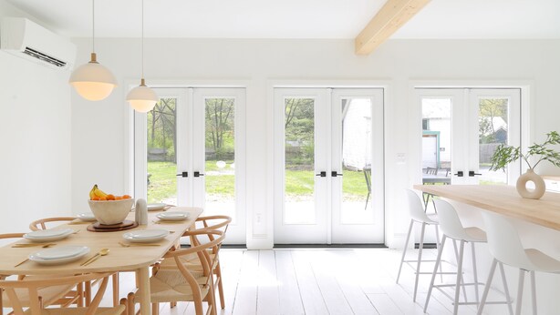 Une cuisine lumineuse et moderne, dotée d’une grande table à manger, de chaises blanches et de luminaires suspendus.