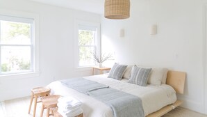 Une chambre lumineuse avec un grand lit, des tabourets en bois et un luminaire suspendu.