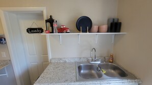 Een keuken met een granieten aanrecht, een roestvrijstalen spoelbak en een hangplank met keukenspullen.