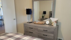 Een slaapkamer met een geruit sprei, een kaptafel met spiegel en een klein horloge.