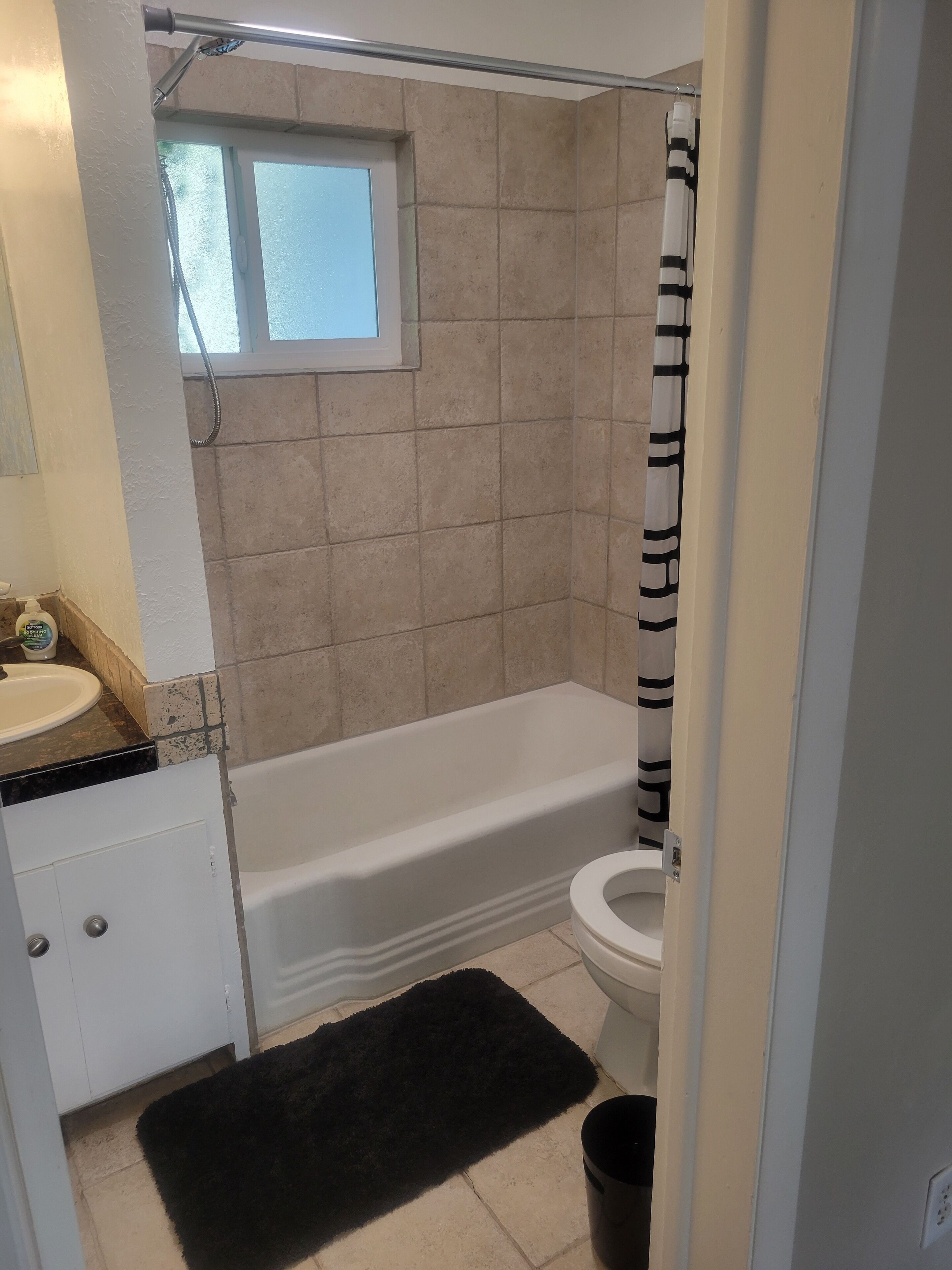 Une salle de bain avec une baignoire, des toilettes et une fenêtre située au-dessus de la douche.