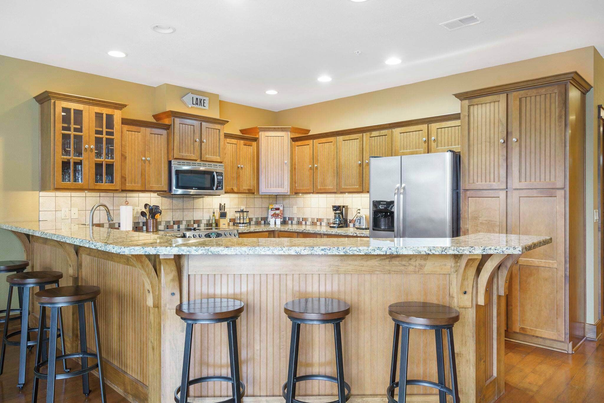 A kitchen with wooden cabinets, a granite countertop, a stainless steel refrigerator, and a built-in island with stools.