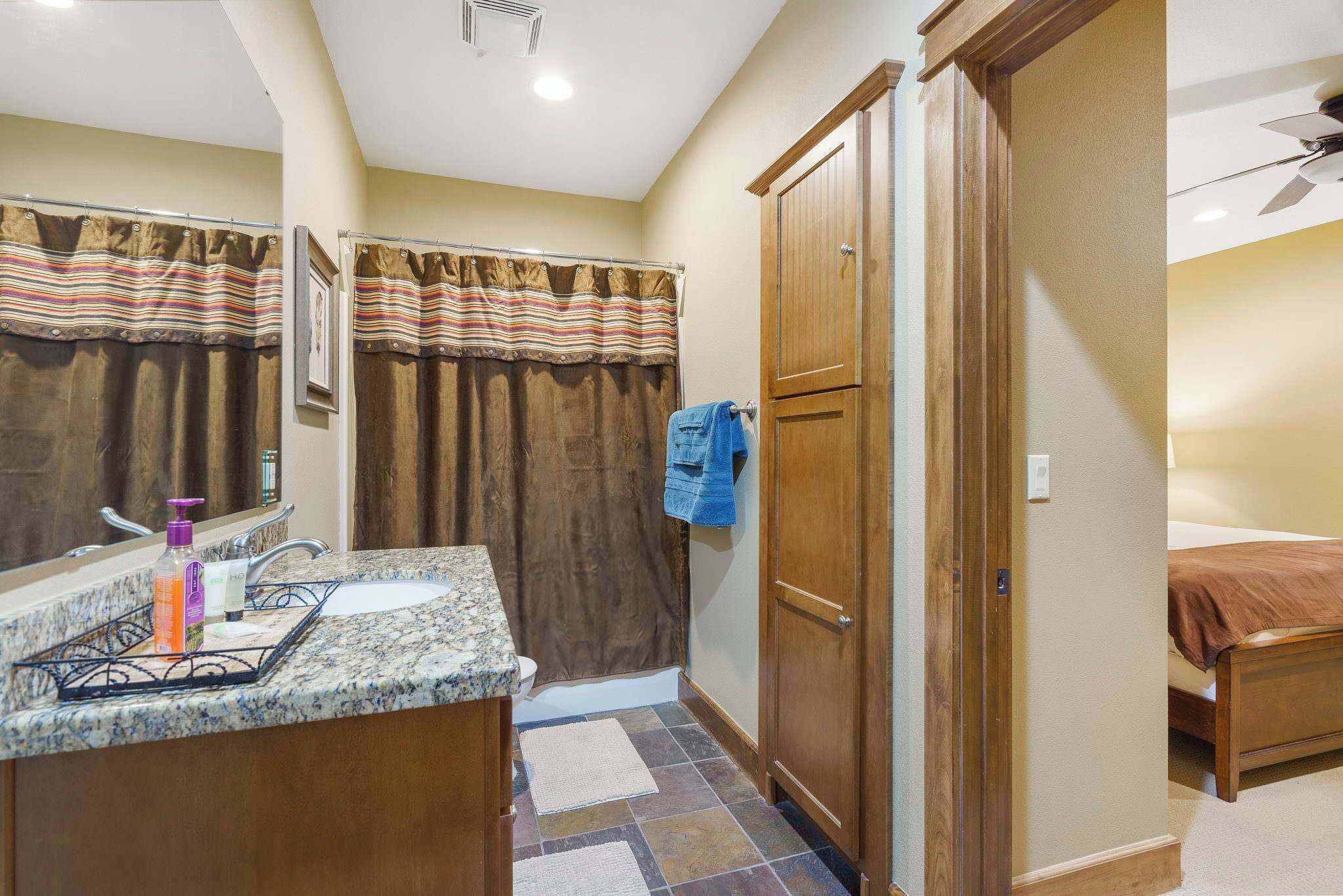 A bathroom with a marble sink, a shower curtain, a wooden door, and a towel hanging on the door.