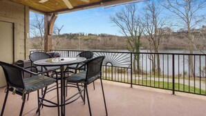 Un espace extérieur aménagé, abrité et doté de tables et de chaises, offrant une vue sur une étendue d’eau et des arbres.