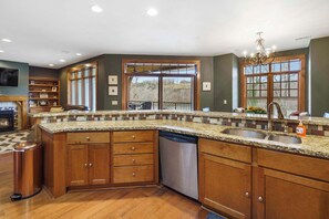 A kitchen with wooden cabinets, granite countertops, a dishwasher, and a large window with a view of trees. - Taneycomo Retreat - Lakefront Condo (Branson)