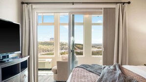 Ett hotellrum med en säng, en TV, ett skrivbord och utsikt över stadsbilden genom stora fönster.