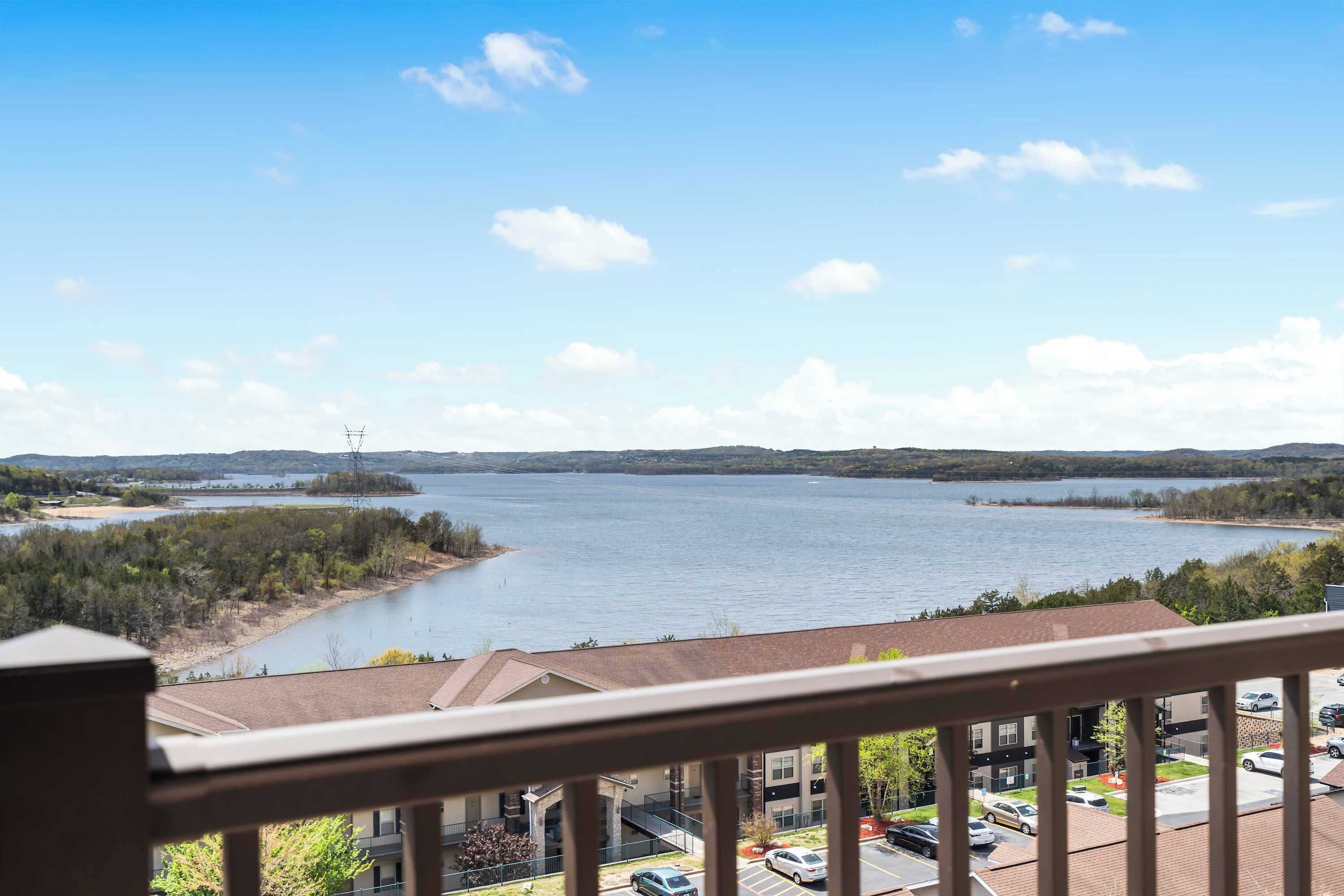 Udsigt fra en balkon over et søområde med bygninger og parkerede biler i forgrunden.
