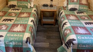 Eine Hütte mit zwei Betten, jedes mit einer 'Cabin sweet Cabin'-Stegdecke, einem kleinen Holztisch mit einer Laterne und einer karierten Tischdecke.