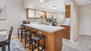 A modern kitchen with a central island, bar stools, and a dining table with chairs. - Skyline View at the Foothills (Branson)