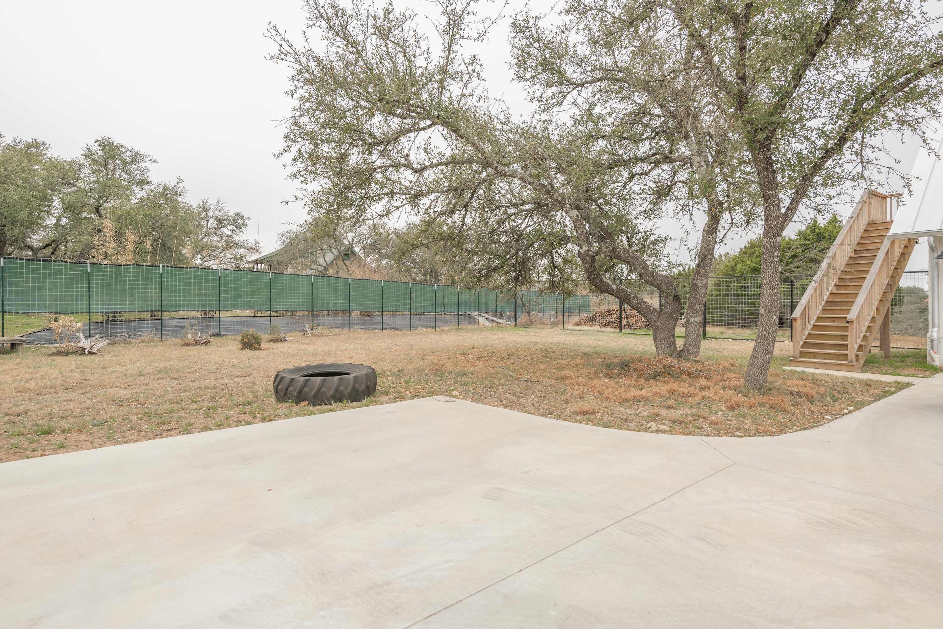 A concrete patio area with a tire, trees, and a wooden staircase.