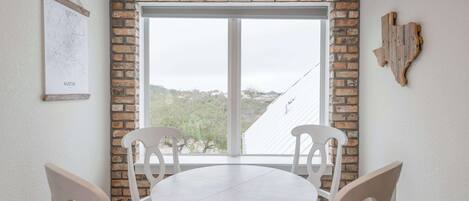 Una habitación con pared de ladrillo, un ventanal grande y una mesa redonda con sillas.