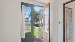 An open door leading to a patio with a view of a blue umbrella and a grassy area.