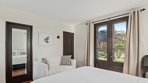 A bedroom with a large bed, a sofa, a door, and a window with curtains.