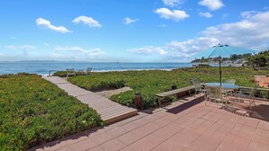 A coastal walkway with a view of the sea, a wooden deck, and outdoor seating.