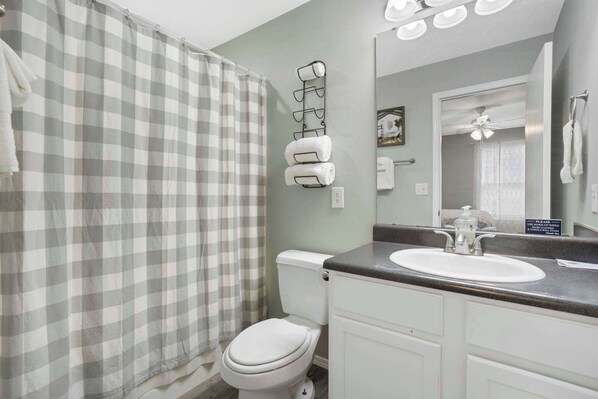 A bathroom with a checkered shower curtain, a toilet, a sink with a mirror, and a towel rack. - Rockwall Lodge - Close to Branson Strip! (Branson)