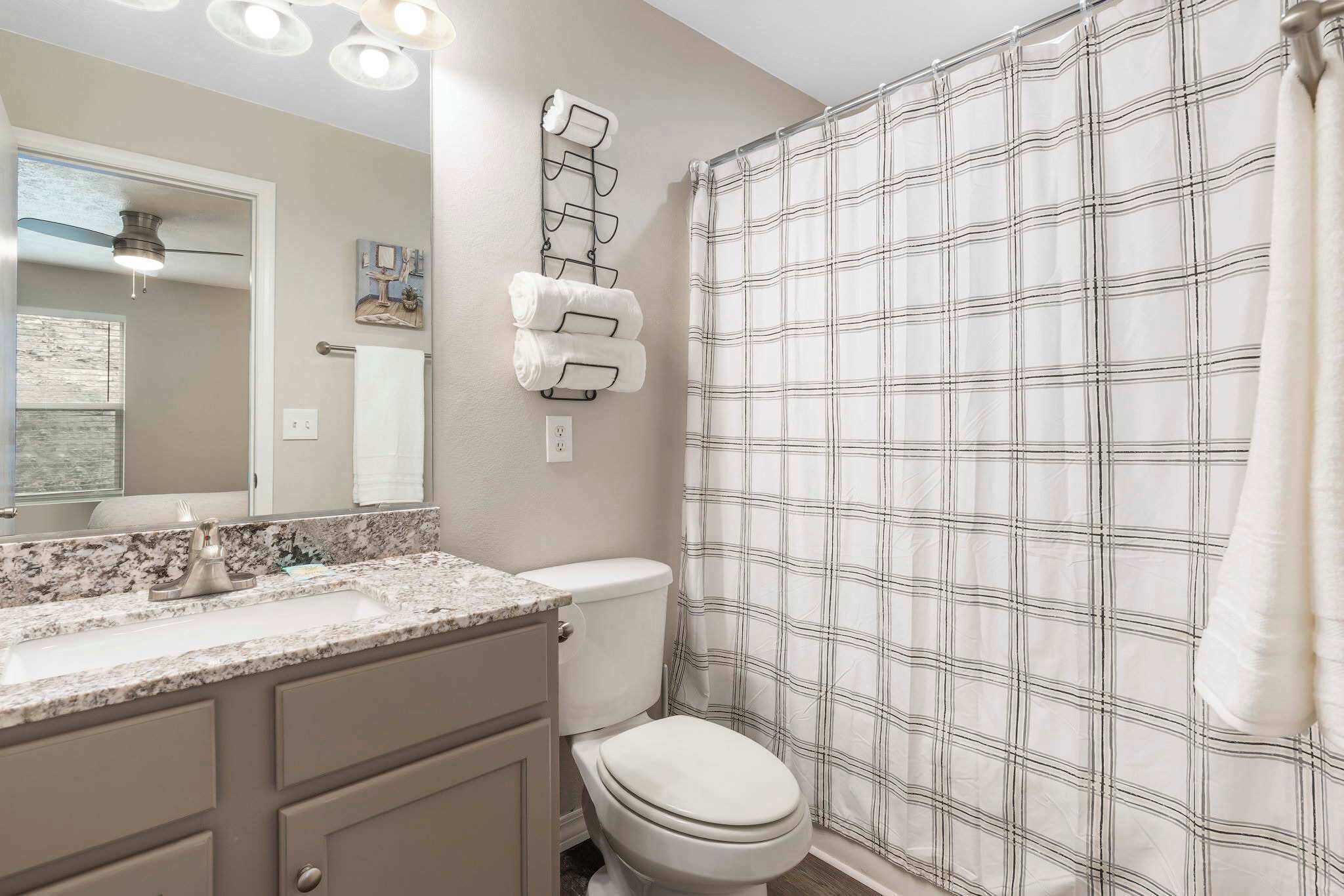 A bathroom with a marble sink, a toilet, a towel rack, and a plaid shower curtain.