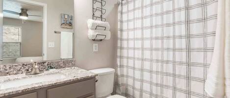 A bathroom with a marble sink, a toilet, a towel rack, and a plaid shower curtain.