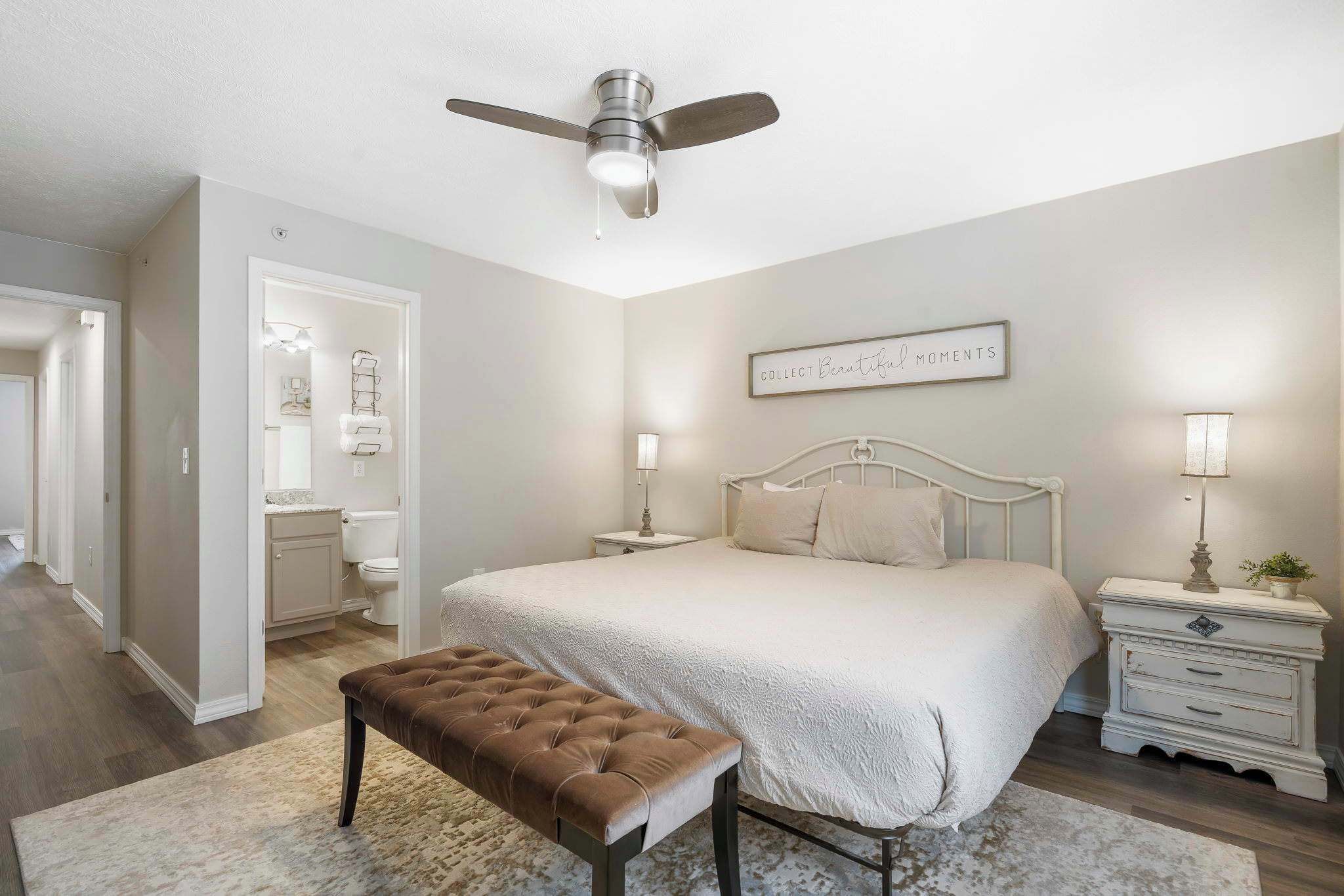 A bedroom with a bed, bedside tables, a ceiling fan, and a bench.
