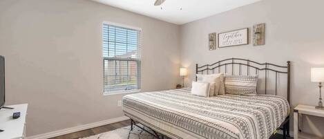 A bedroom with a bed, a ceiling fan, a window, and a nightstand with a lamp.