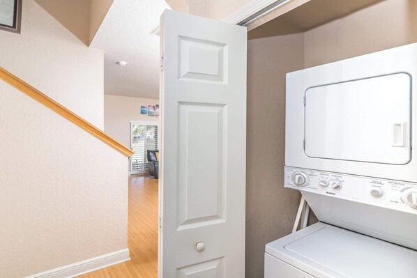 A laundry room with a white washer and dryer, a wooden staircase, and a door leading to another room. - Rendezvous at Regal Palms (Davenport)