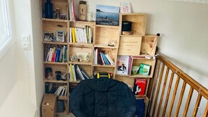 Une pièce avec une bibliothèque en bois remplie de livres et d’objets décoratifs, une chaise noire, un tapis blanc et une rambarde en bois.