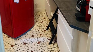 Une cuisine de taille réduite avec un réfrigérateur rouge, un sol carrelé et un plan de travail sur lequel se trouve un mixeur.