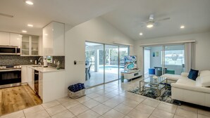 Een moderne keuken met een magnetron, kookplaat en spoelbak, een woonehoek met een bank en salontafel, en een schuifpui naar een zwembad.